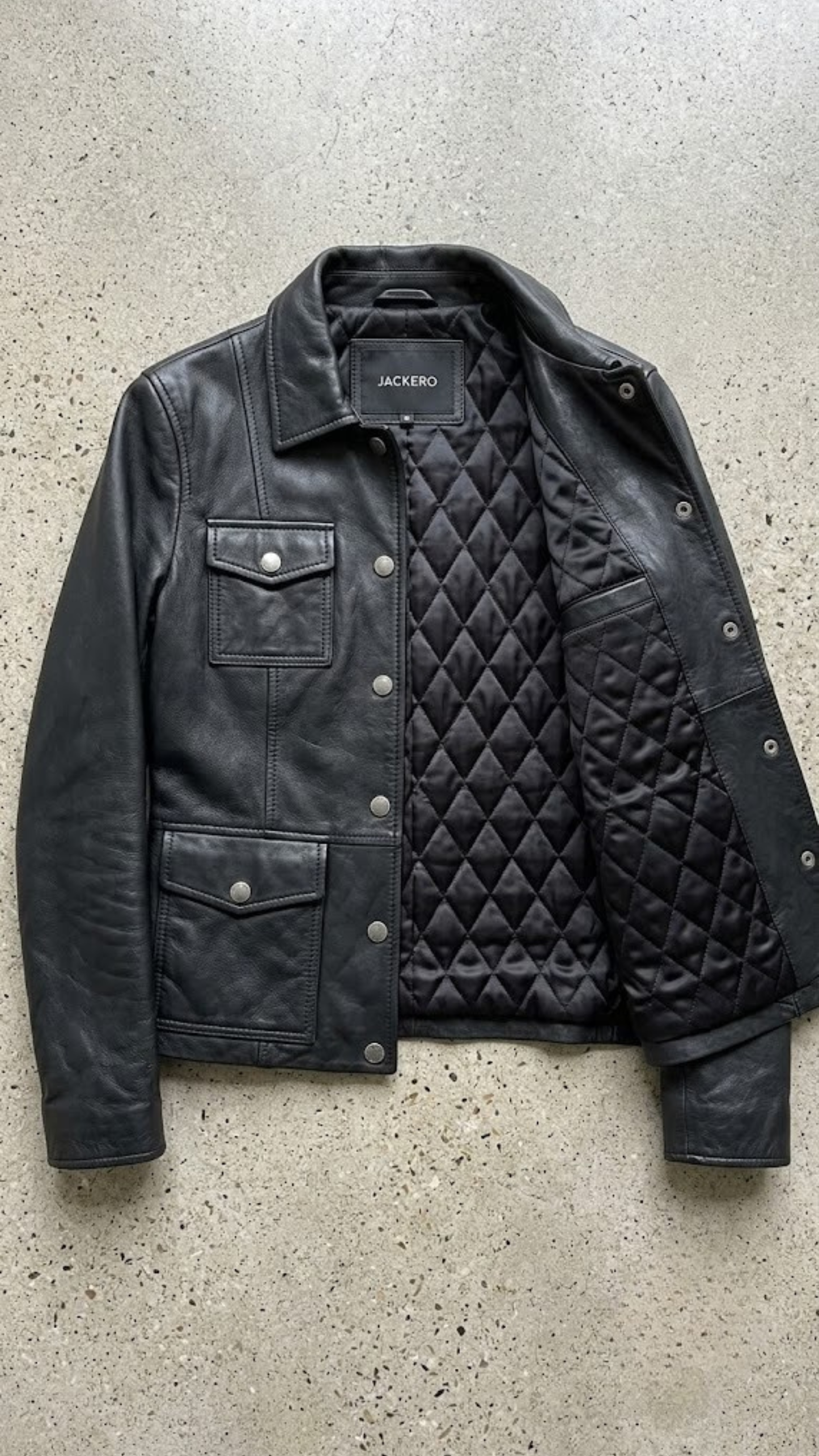 Jacker jacket flat lay presentation featuring the contemporary matte black leather shirt-collar jacket neatly displayed on a studio backdrop.