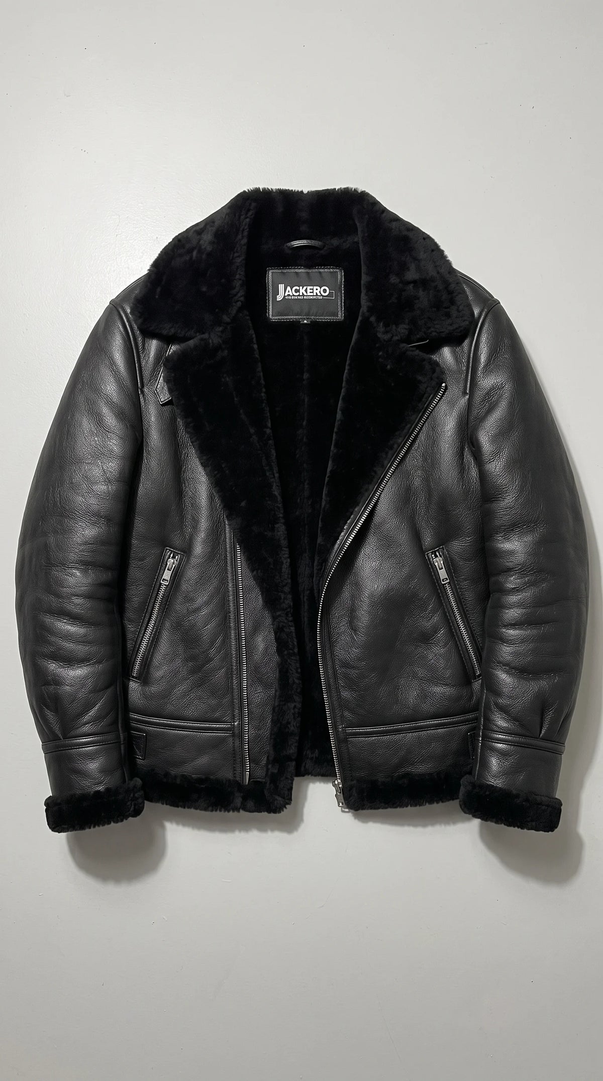 Black grain-finish leather aviator jacket displaying its JACKERO neck label, plush black faux-shearling interior, oversized fold-down collar, diagonal silver front zipper and matching shearling-trimmed cuffs and hem for a cohesive luxury winter design.
