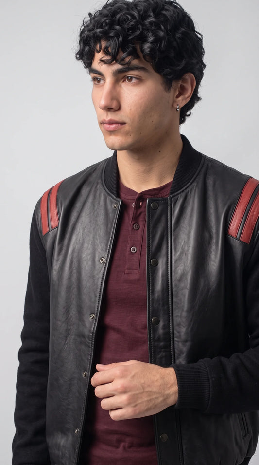 Close-up of a black leather and suede varsity bomber jacket featuring double red shoulder stripes, a ribbed baseball collar and a neat row of metal snap buttons. The contrasting textures and carefully defined panels give this men’s statement outerwear a motorsport-inspired edge, ideal for shoppers looking for distinctive black and red jacket detailing.