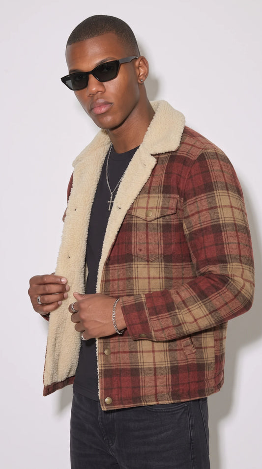 Close-up of a burgundy-red and tan plaid cotton jacket featuring a high-pile cream faux-shearling collar, intersecting checked lines, button-fastened chest pocket flaps and sturdy metal shank buttons, showcasing the contrast between woven flannel texture and plush winter lining.