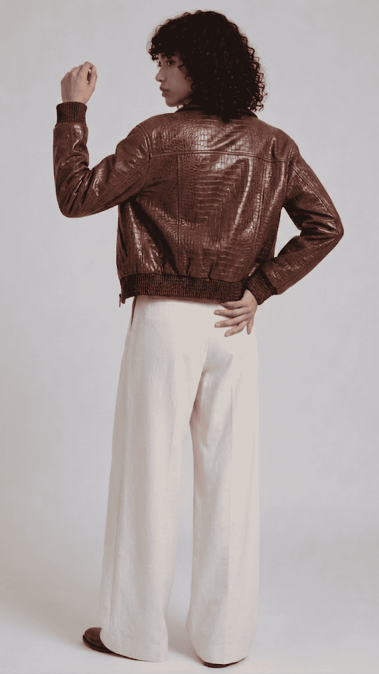 Model wearing a brown croc-embossed leather jacket over a black henley shirt paired with off-white wide-leg trousers.