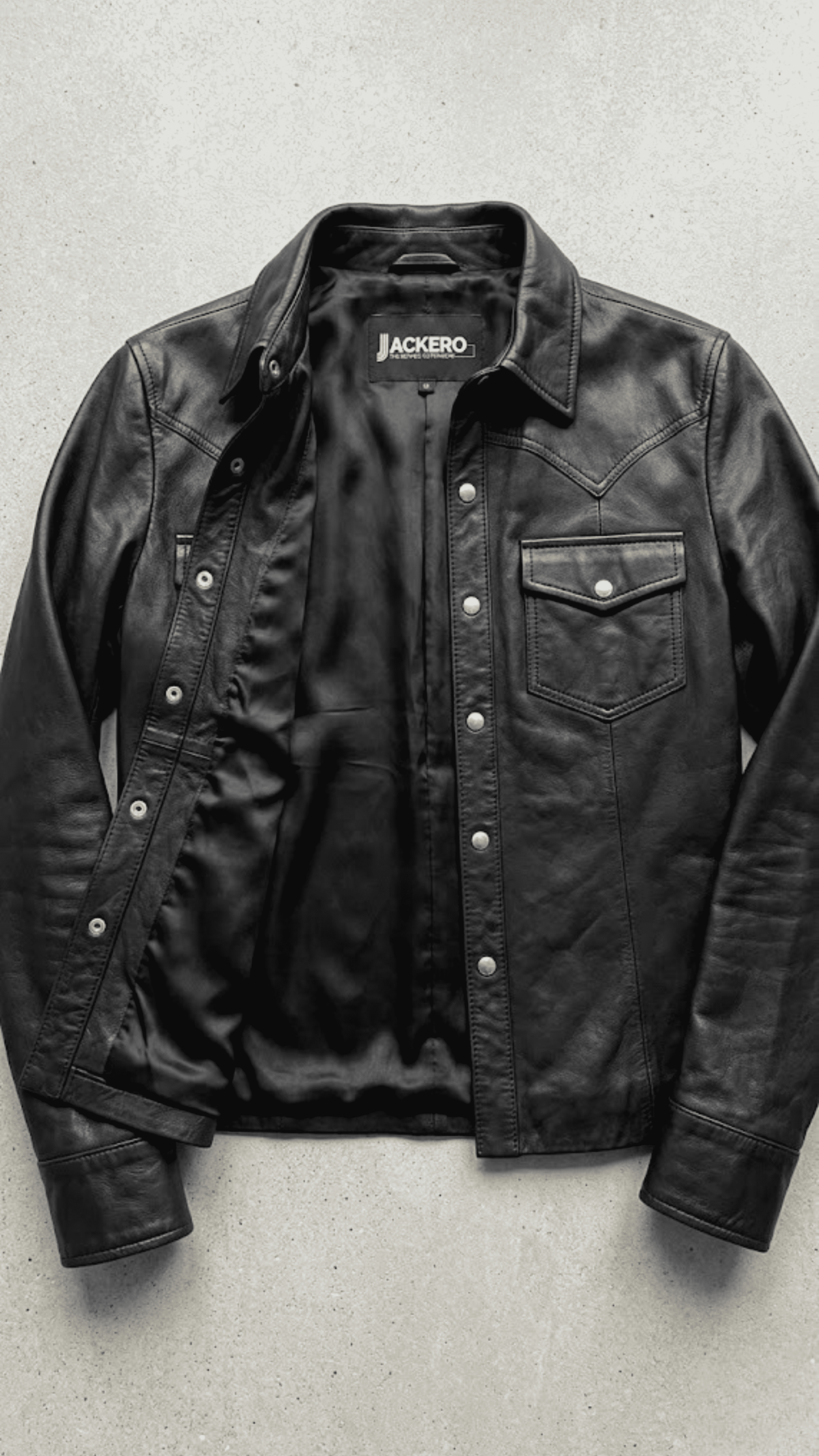Jackero jacket flat lay photography of a high-end black leather shirt-style trucker coat displayed on a solid grey backdrop.