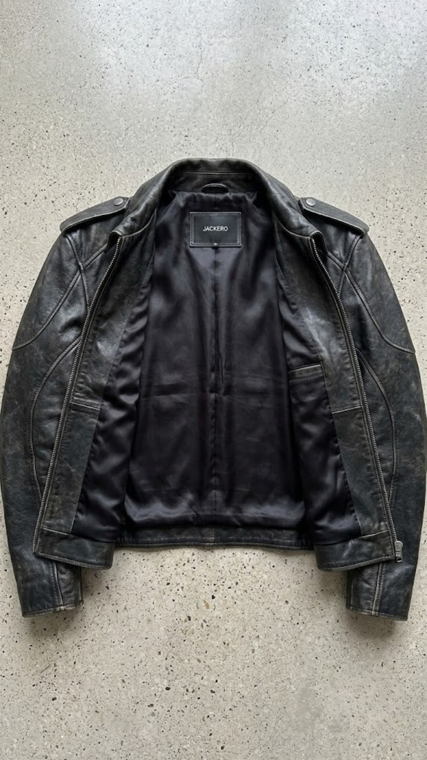 flat lay photography of a high-end vintage wash black leather café racer coat on a solid neutral backdrop.
