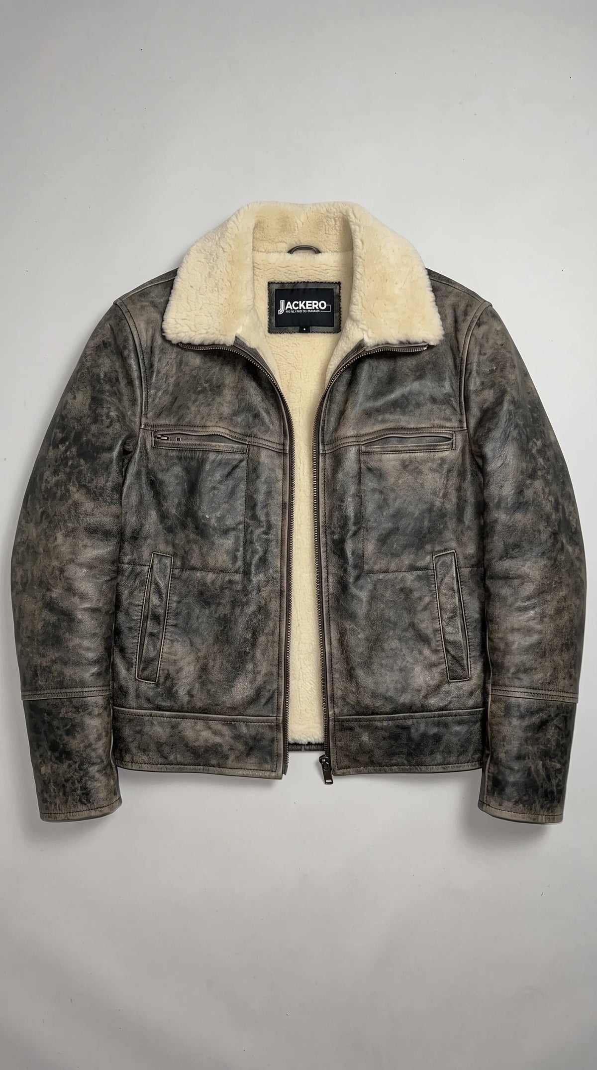 JACKERO dark-grey distressed genuine leather jacket displayed open to reveal its plush cream interior, white faux-shearling collar and signature neck label, with dual zipped chest pockets, a full-length industrial metal zipper and carefully reinforced leather panel construction.