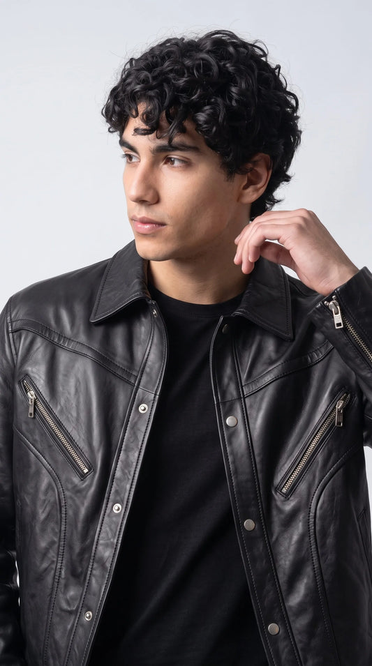 Close-up of a jet-black genuine leather jacket featuring two angled chest pockets with polished metal zippers, a classic pointed collar and a row of silver snap buttons along the front placket. The softly reflective leather grain and sweeping curved seams give this oversized men's jacket a distinctive architectural look, combining practical pocket design with refined biker-inspired detailing.