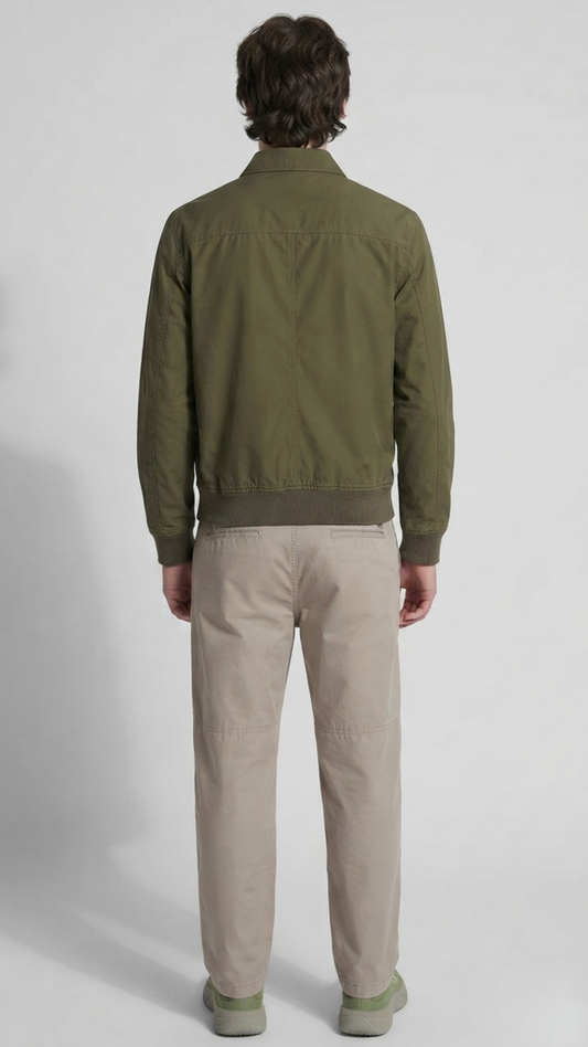 A man viewed from the back wearing an olive green jacket and beige trousers, standing against a light gray studio background.