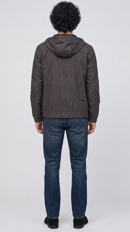 A man viewed from behind wearing a dark gray hooded jacket and blue jeans, standing against a light gray studio background.