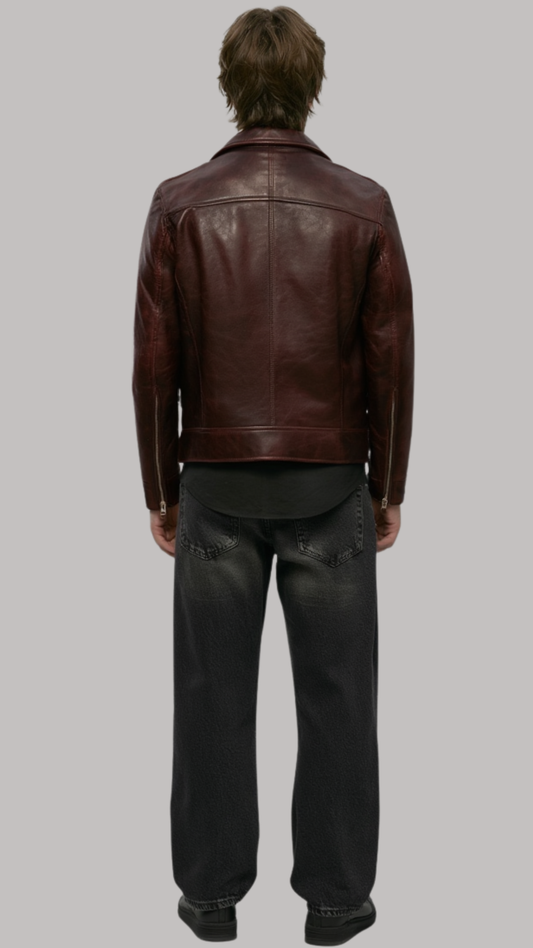 A man viewed from behind wearing a dark brown leather jacket, a black t-shirt, and black jeans, standing against a solid gray background.