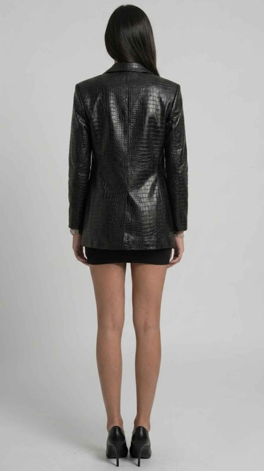 A model shown from the back wearing a black textured croc leather blazer, a short black skirt, and black high heels against a light gray studio background.