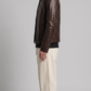 Man wearing a brown textured jacket and beige pants on a gray background