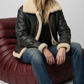 Clean studio photography of a men's luxury black genuine leather coat featuring a striking faux cream shearling trim.