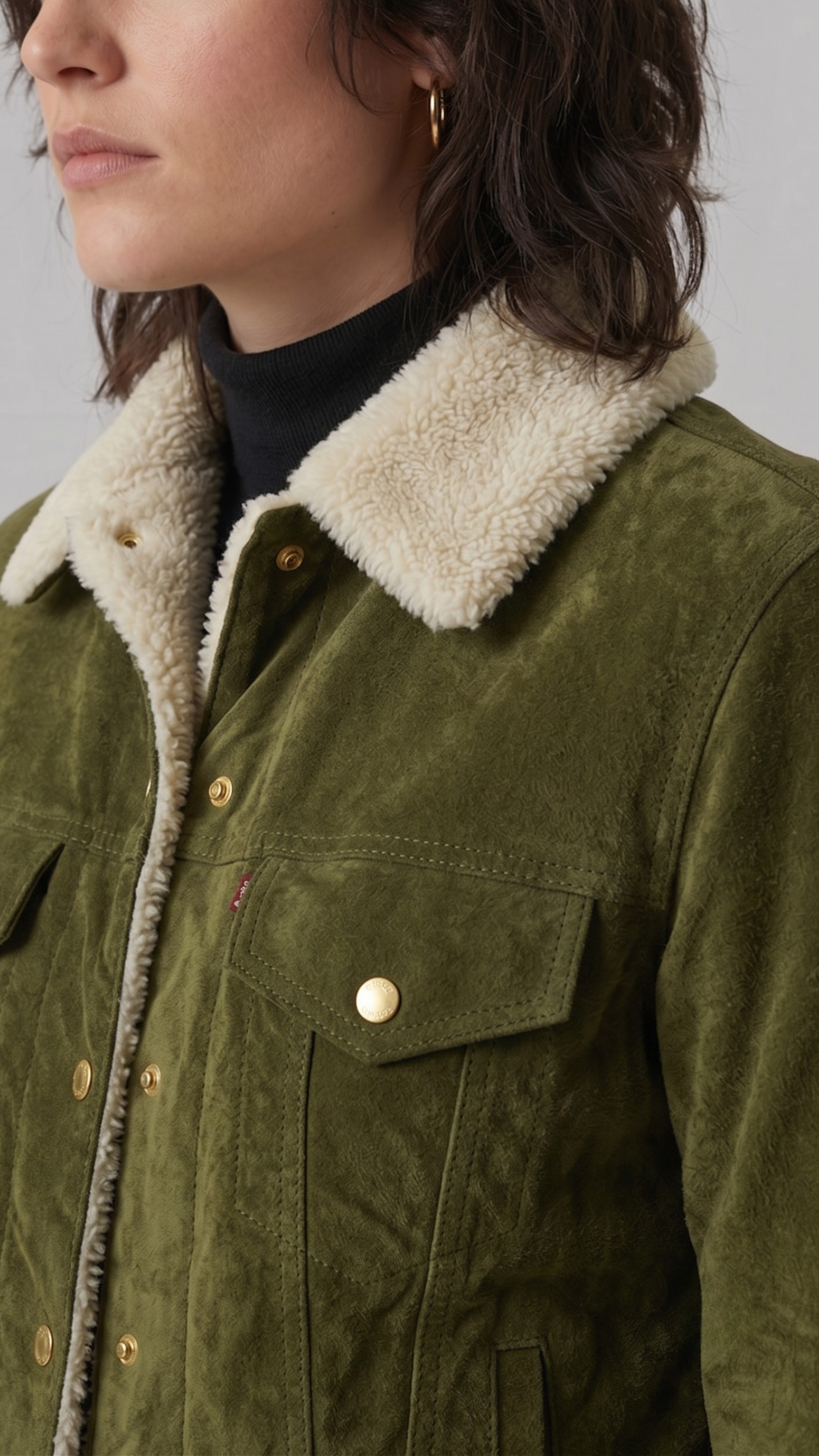 Close-up of a person wearing a green jacket with a beige sherpa lining on a neutral background