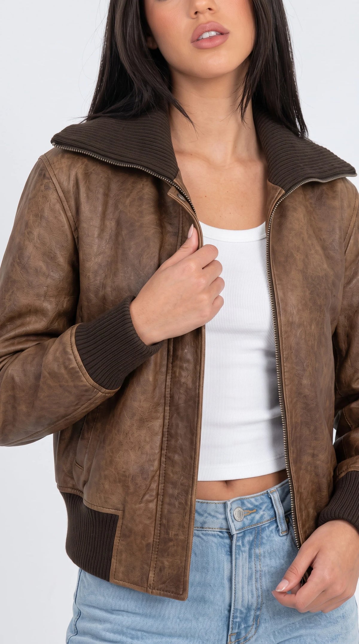 Aged chocolate brown leather flight jacket with knit collar and cuffs, paired with low-rise blue jeans and a white crop top