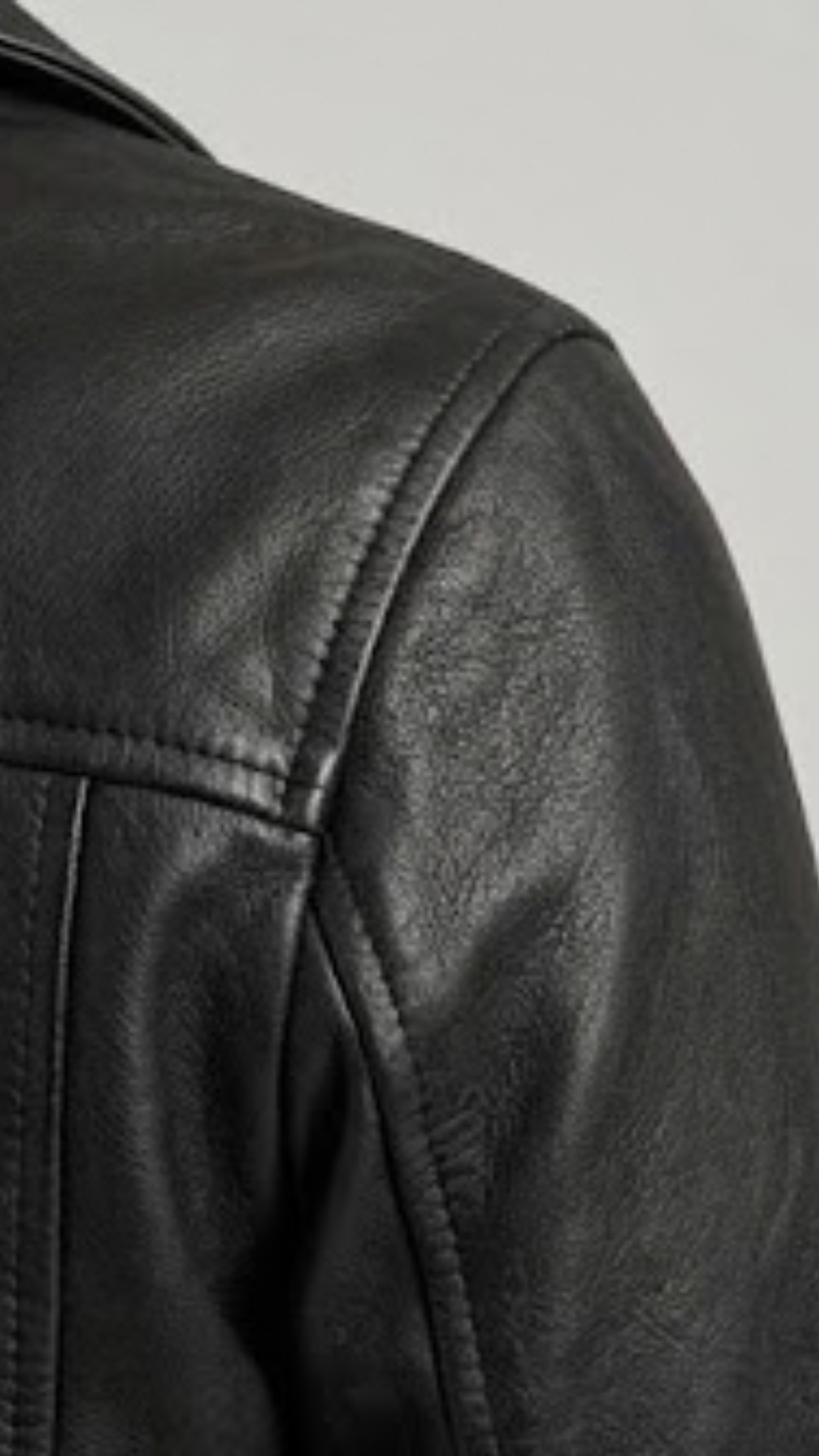 Detailed shot of high-quality stitching, premium hardware, and textured genuine black leather on a classic biker jacket silhouette.