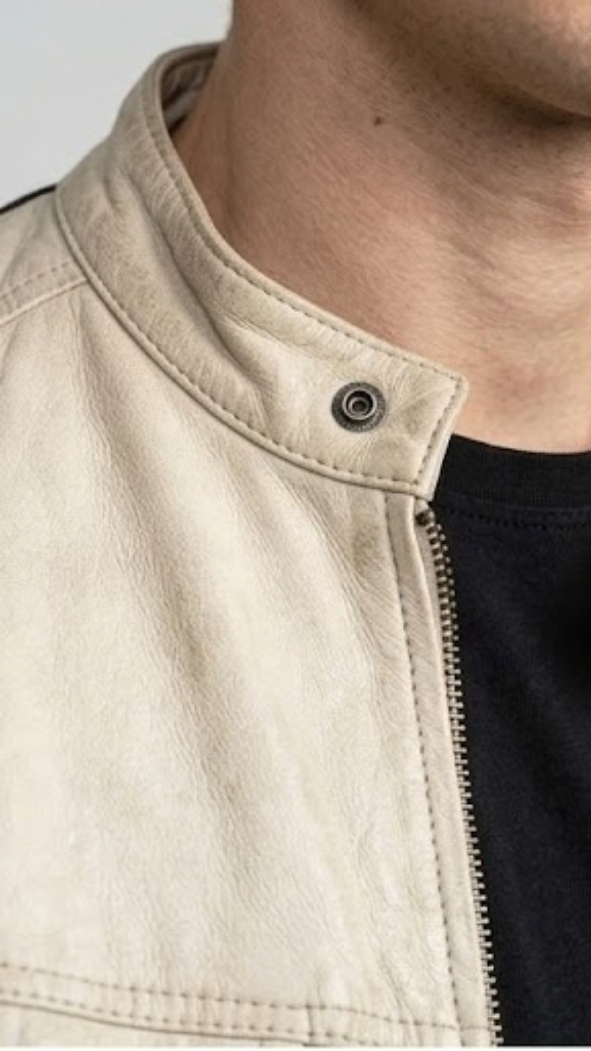 Macro detailed focus capture showing the smooth premium ivory grain texture and sleek silver hardware accents on the off-white leather jacket.