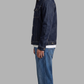 Man wearing a dark blue denim jacket and jeans on a gray background