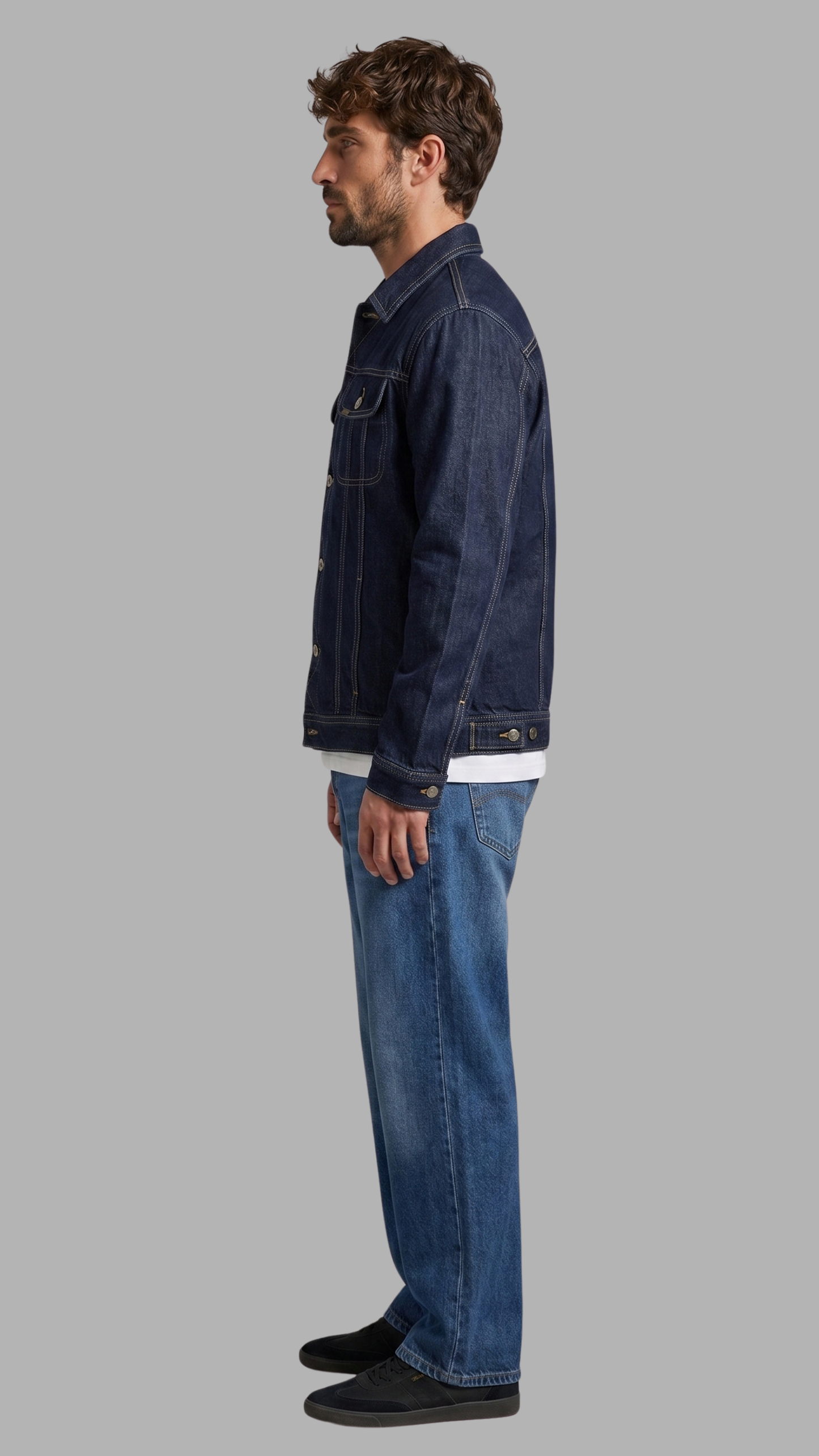 Man wearing a dark blue denim jacket and jeans on a gray background