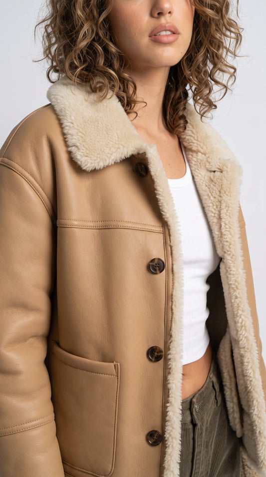 Modern beige leather jacket with contrasting cream shearling edging and dark horn-style buttons, creating a relaxed minimalist streetwear look for everyday cold-weather outfits.