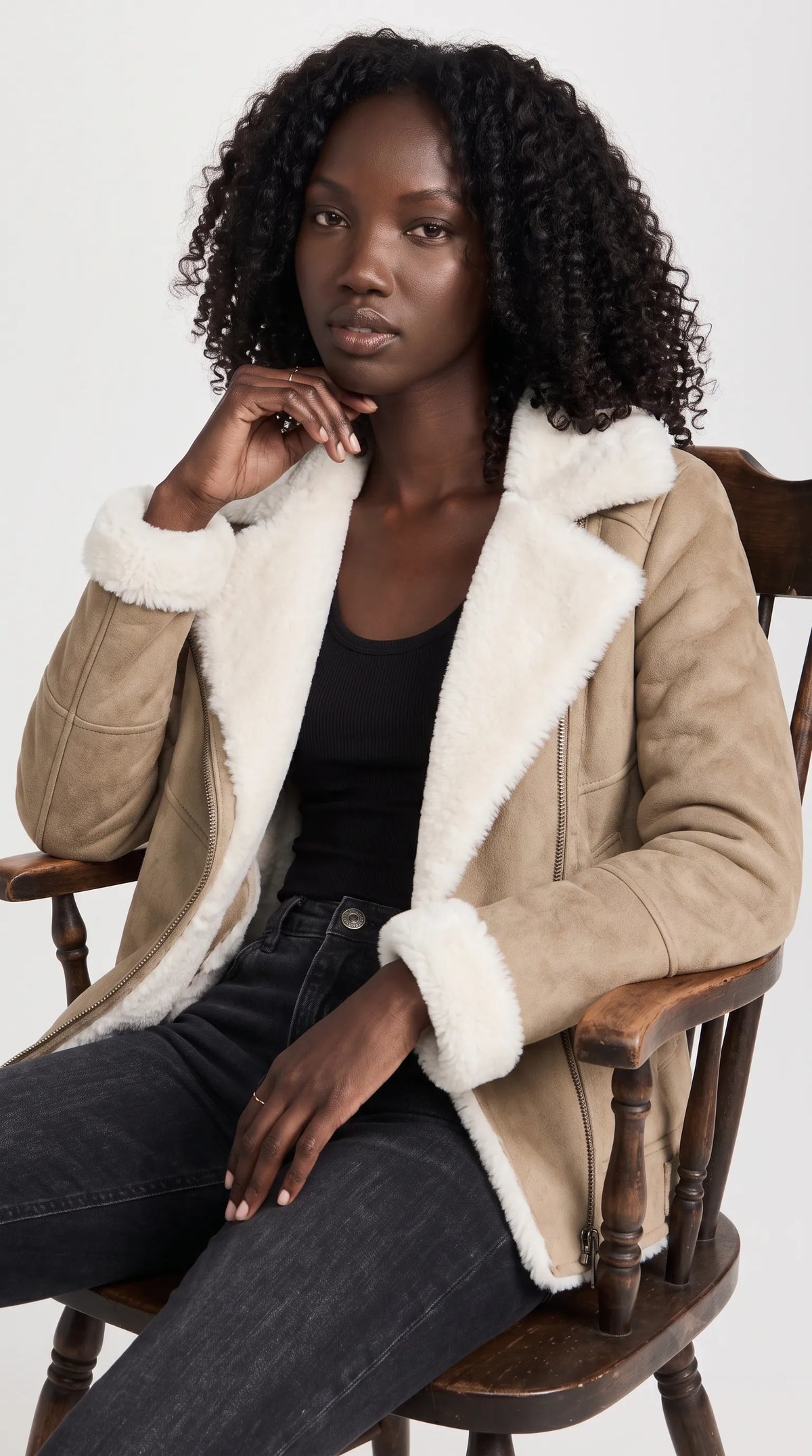 A beige genuine suede aviator jacket with a voluminous ivory shearling lining is styled open over a simple black top and charcoal-black jeans for an effortless luxury casual look. Its contrasting textures, broad collar and diagonal fastening make it ideal inspiration for relaxed weekend outfits, winter city wear and modern minimalist fashion.