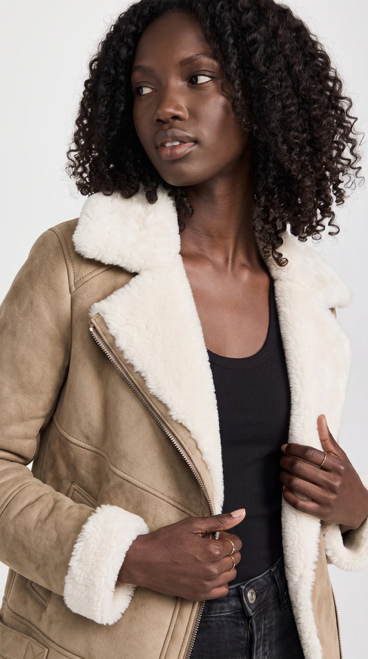 This beige suede moto jacket showcases a soft matte leather texture, oversized ivory shearling lapels, a diagonal metal zip and thick fluffy cuff accents. The contrasting materials create an elevated aviator look for stylish winter layering, premium casual outfits and modern cold-weather fashion.