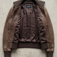 Professional e-commerce product flat lay featuring the premium deep brown leather bomber coat perfectly aligned on a neutral studio background.