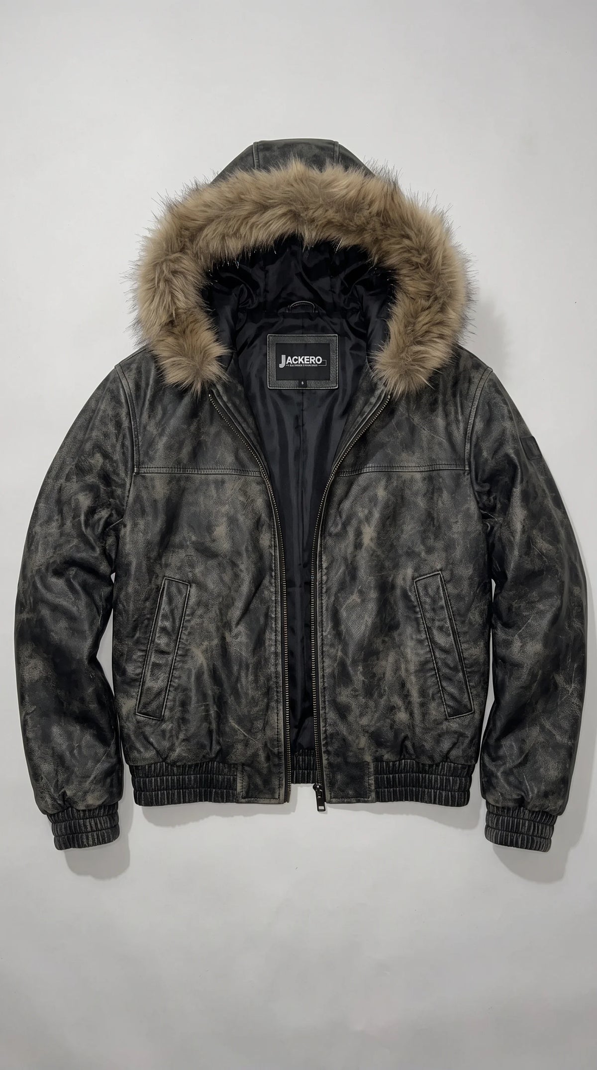 Black acid-washed genuine leather bomber jacket opened to reveal its smooth black satin-finish lining and JACKERO neck label, framed by a voluminous brown faux-fur hood, dark metal zipper and structured rib-knit trims.