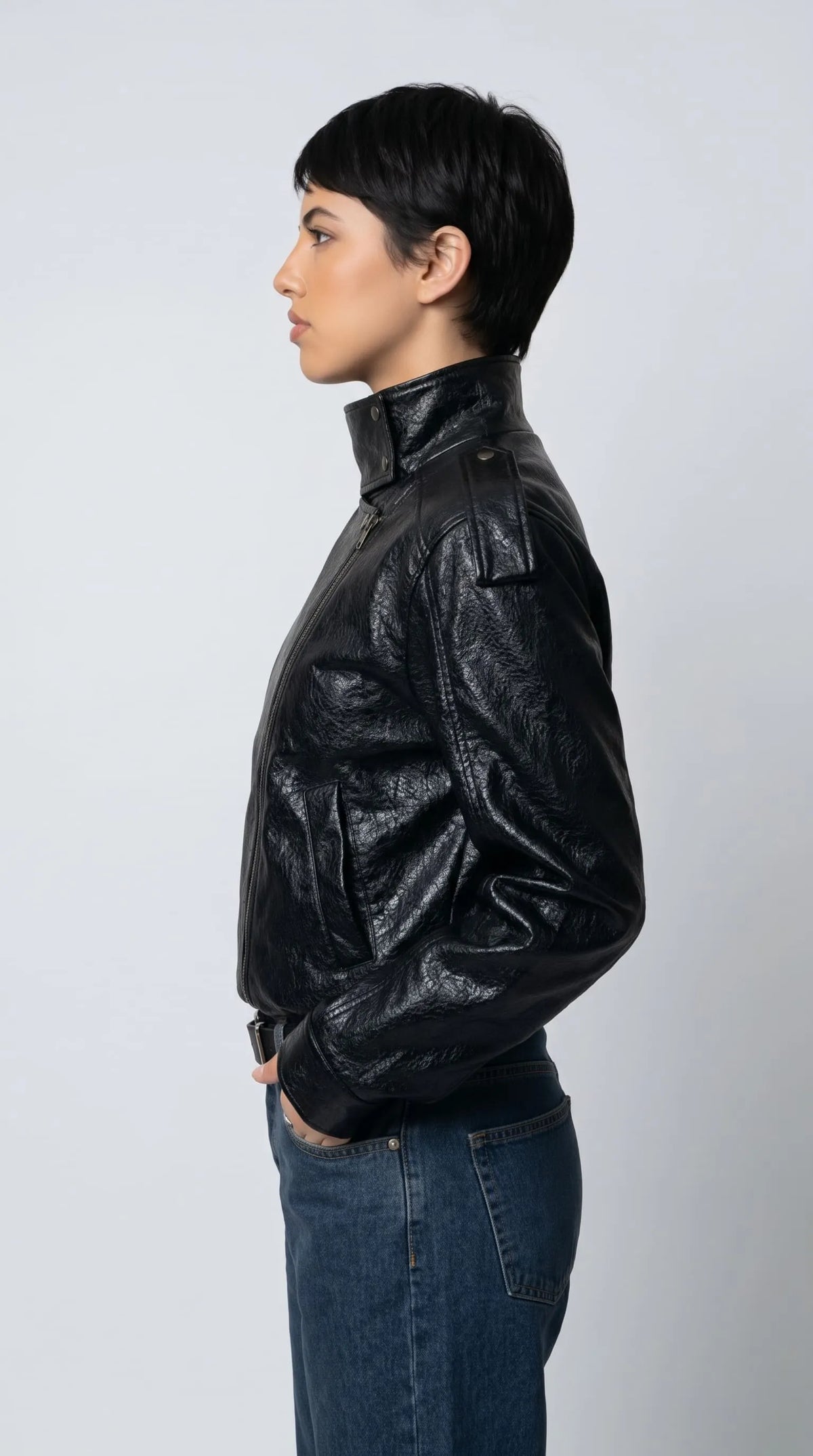 A relaxed black leather high-neck jacket with dropped shoulders, shoulder epaulettes and voluminous sleeves, styled with classic blue jeans for a contemporary urban outfit with a strong minimalist fashion statement.