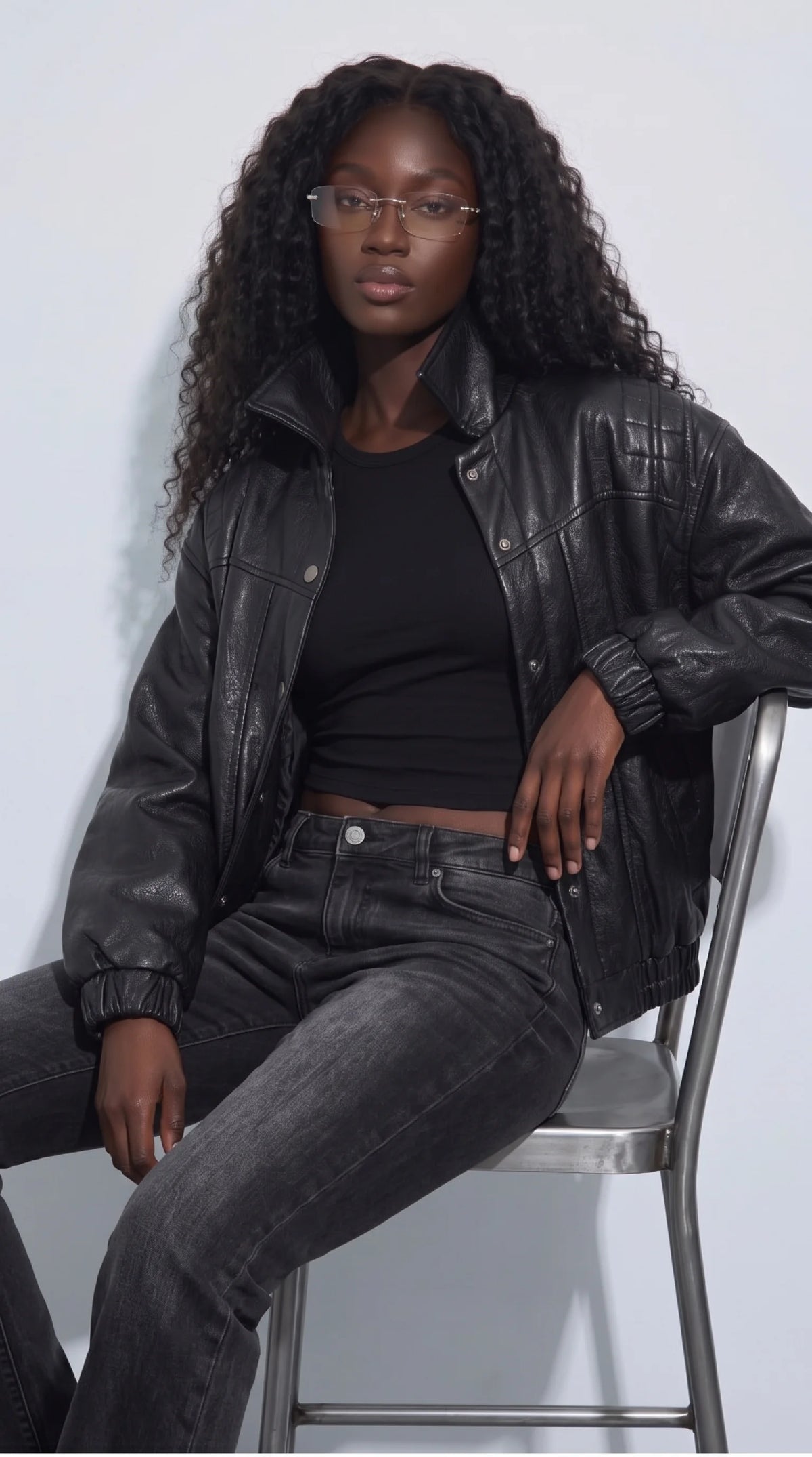 Relaxed editorial outfit featuring a black cropped genuine leather jacket paired with a fitted black top and washed charcoal jeans. The textured leather, quilted shoulders, snap-front fastening and gathered cuffs give the jacket a distinctive shape while keeping the outfit effortlessly wearable, ideal for contemporary women’s streetwear, casual evenings and understated fashion styling.