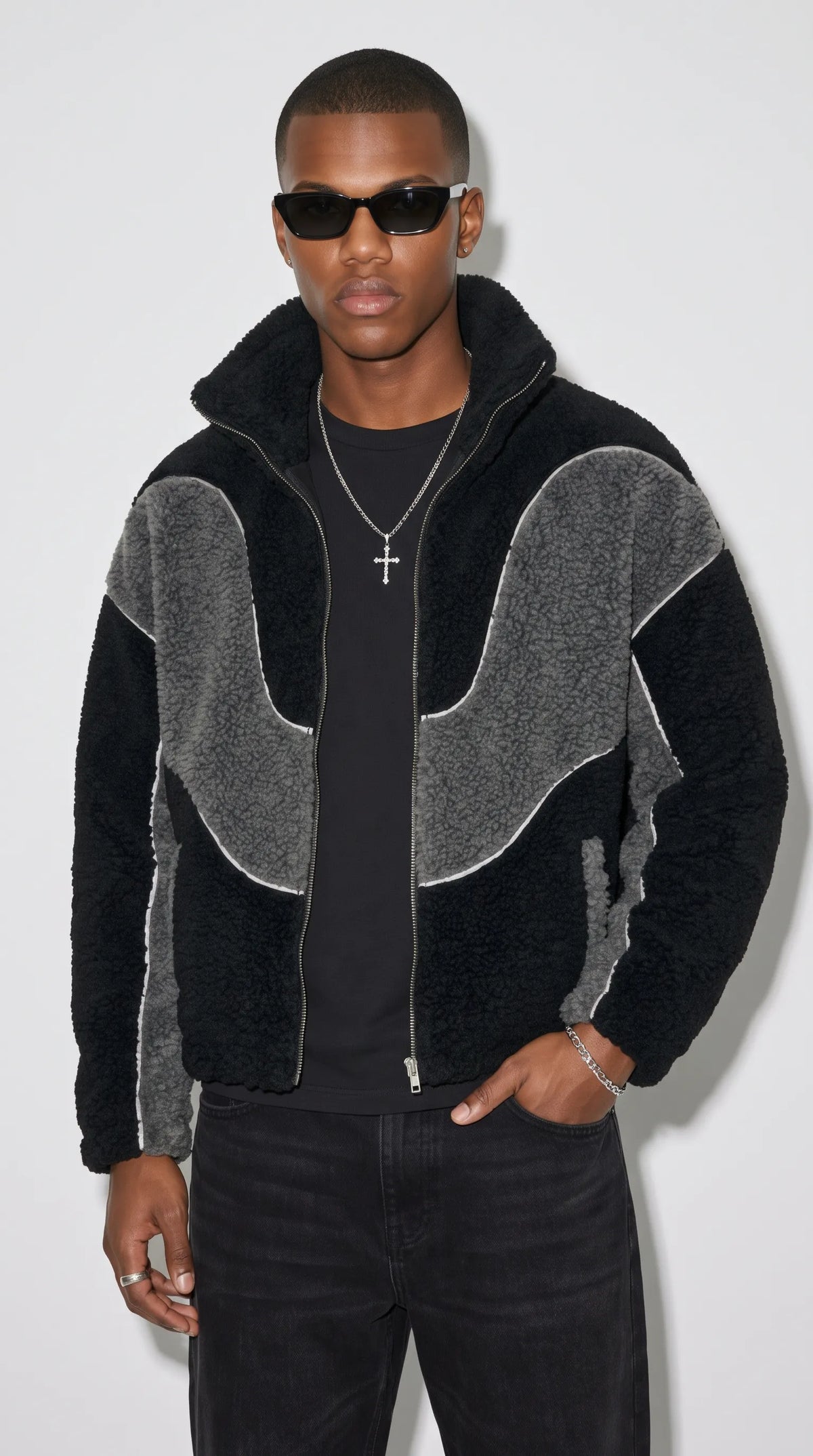 Men’s oversized black and dark grey Y2K jacket crafted from textured wool-blend fleece, featuring sculpted grey contrast panels, fine white piping and a high stand-up collar. Styled with a black T-shirt, dark jeans, sunglasses and silver jewellery, this statement piece brings a bold retro-futuristic streetwear aesthetic to everyday urban fashion.