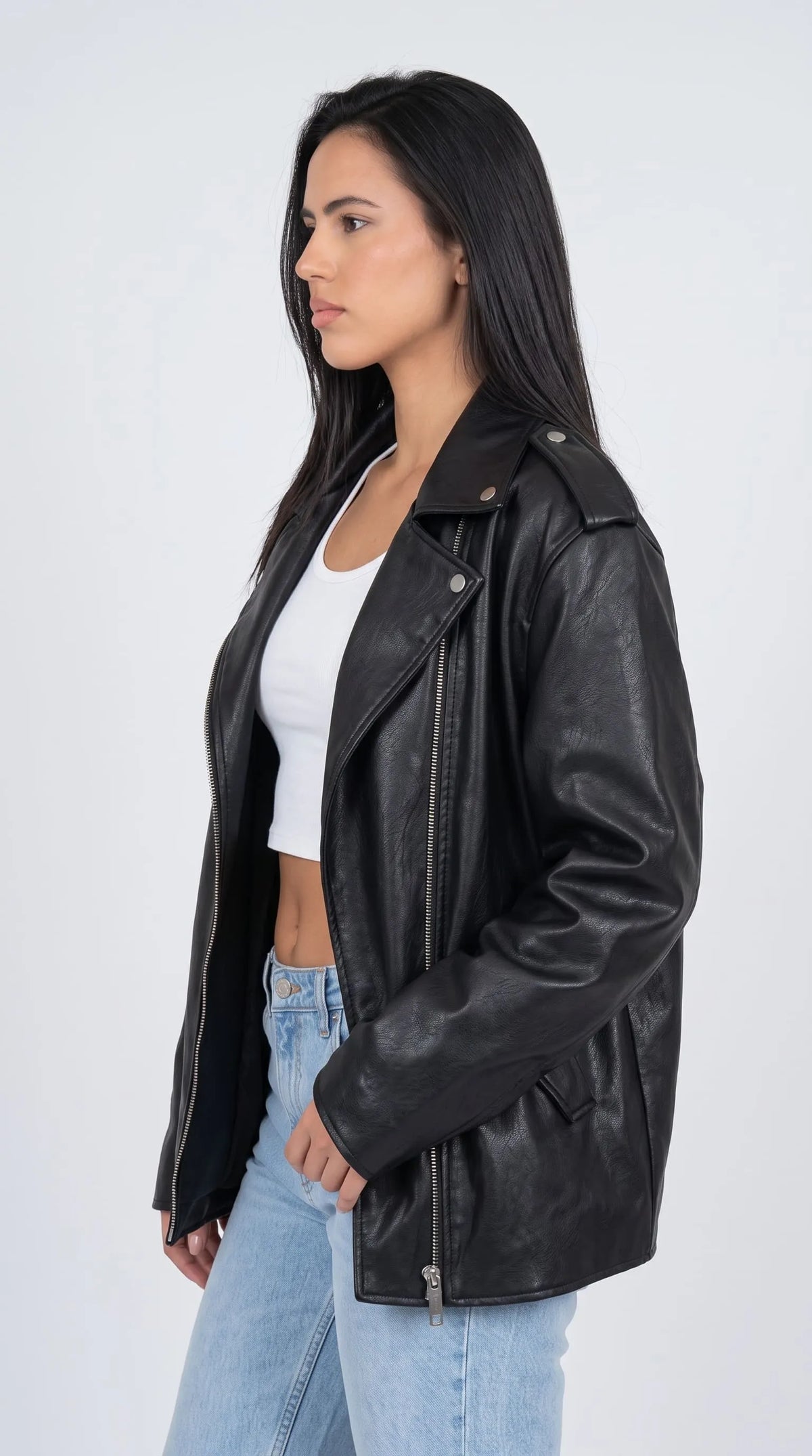 Black genuine leather aviator-style jacket with wide notched lapels, snap-detail shoulder tabs, long relaxed sleeves and an asymmetrical silver front zipper, styled with a white top and light-wash jeans. The oversized cut and rich black leather finish create a strong silhouette for modern city dressing, alternative street style and effortless casual layering.