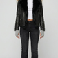 A professional studio shot of the Jackero black leather biker jacket featuring a plush black faux fur collar, styled open over a clean grey backdrop.