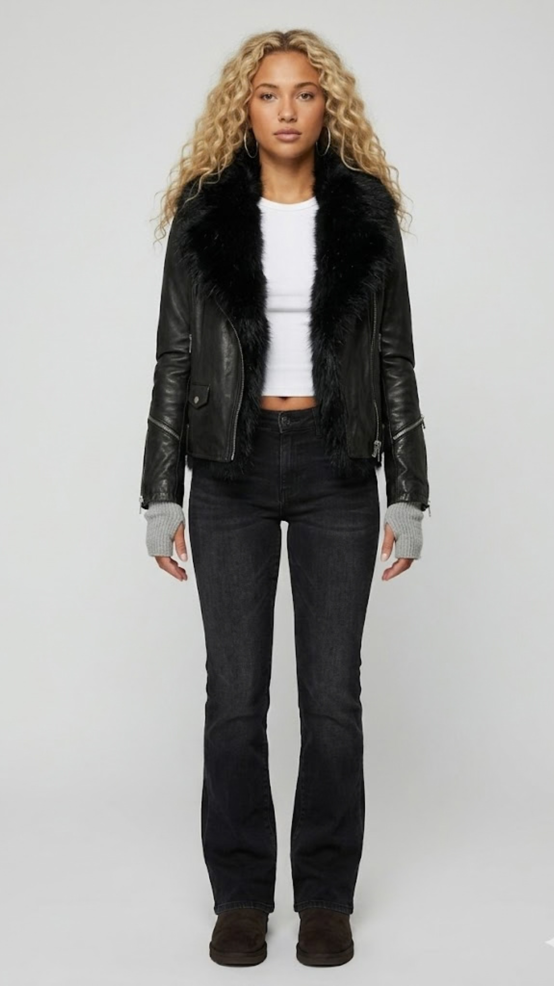 A professional studio shot of the Jackero black leather biker jacket featuring a plush black faux fur collar, styled open over a clean grey backdrop.
