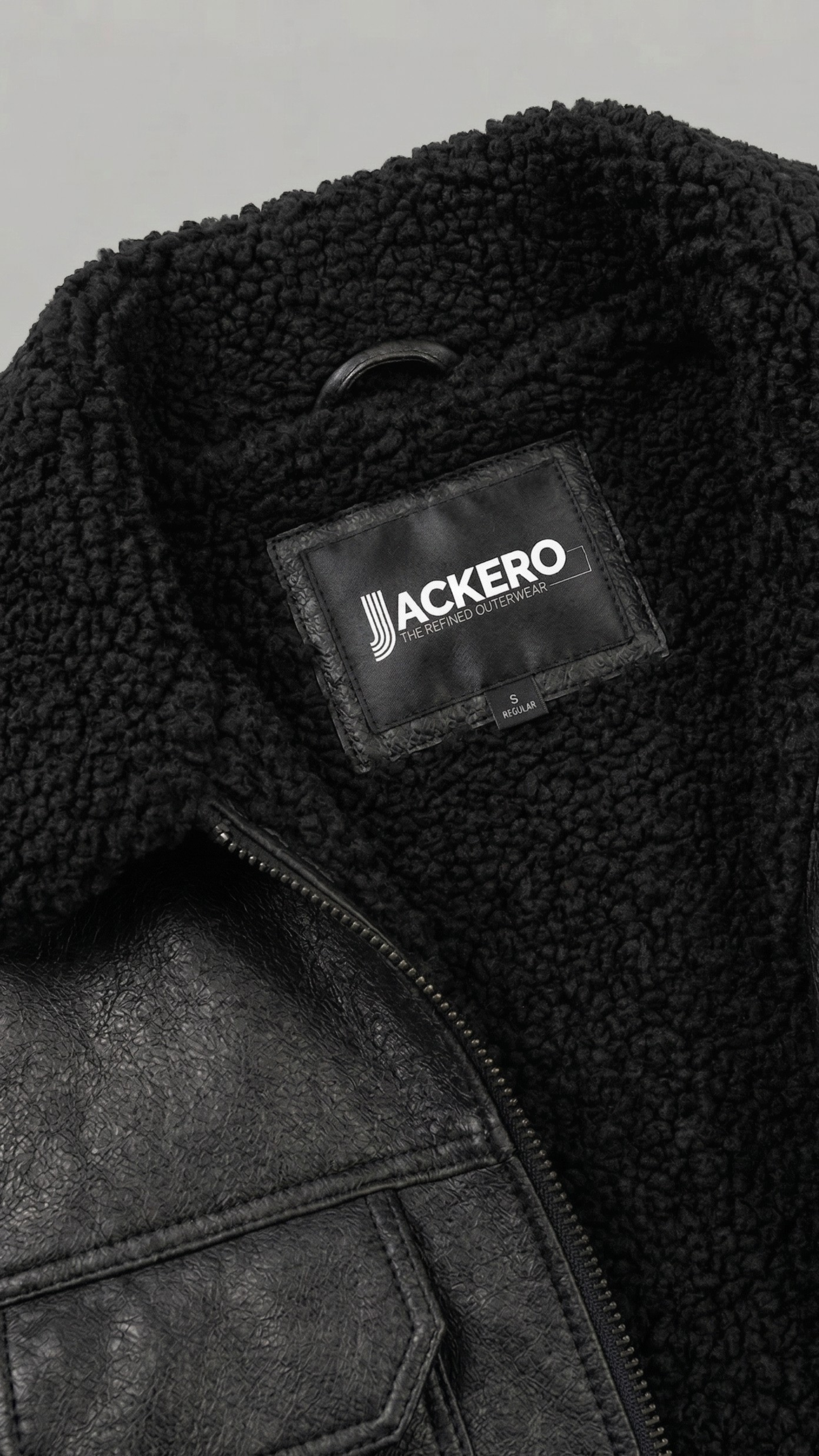 Black leather jacket with black shearling with a visible brand label on a gray background
