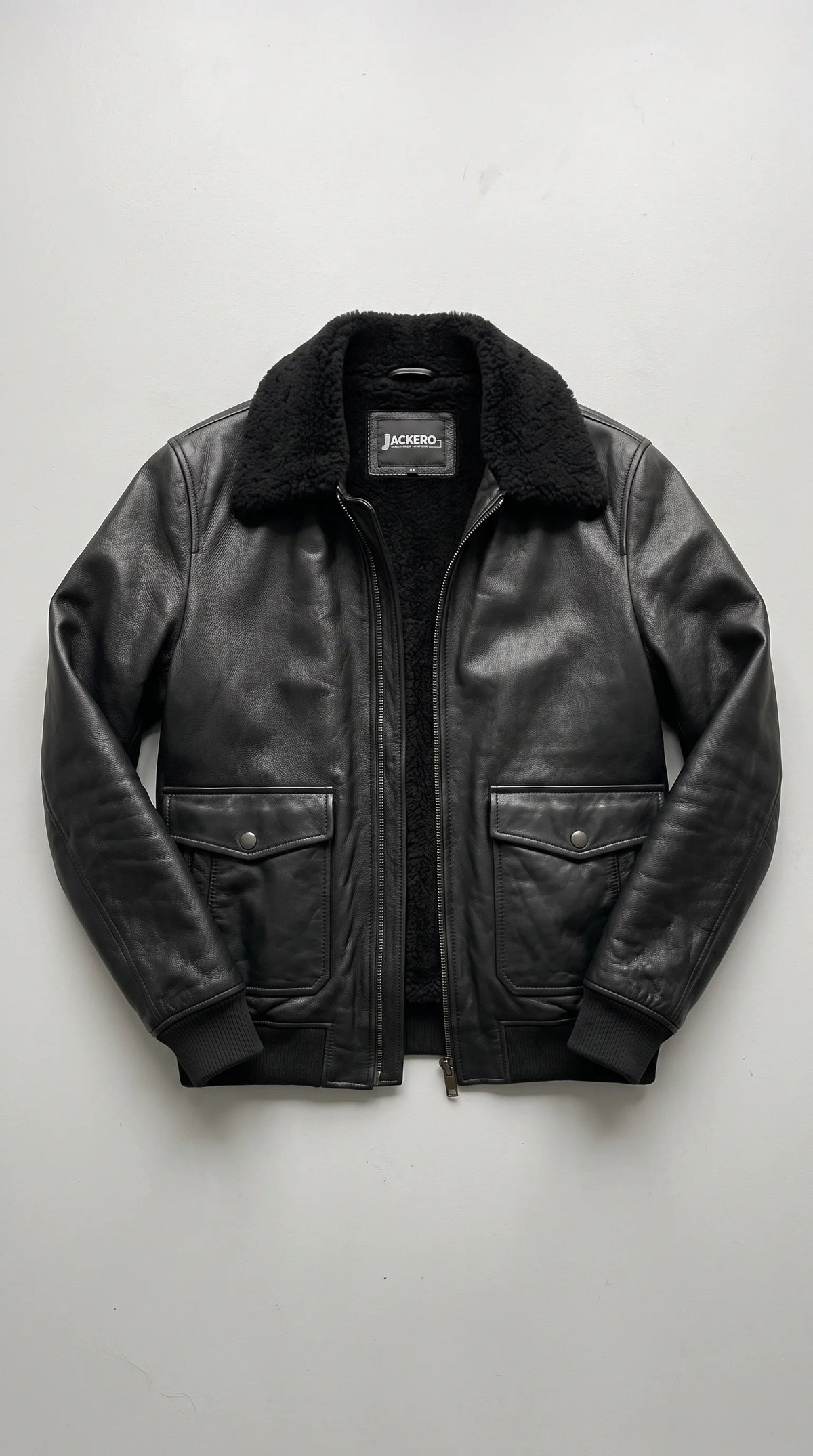 Black genuine leather flight bomber displayed open to reveal its plush black faux-shearling interior and JACKERO neck label, with a full-length metal zipper, two button-flap cargo pockets, smooth leather panels and rib-knit cuffs completing its tonal winter design.