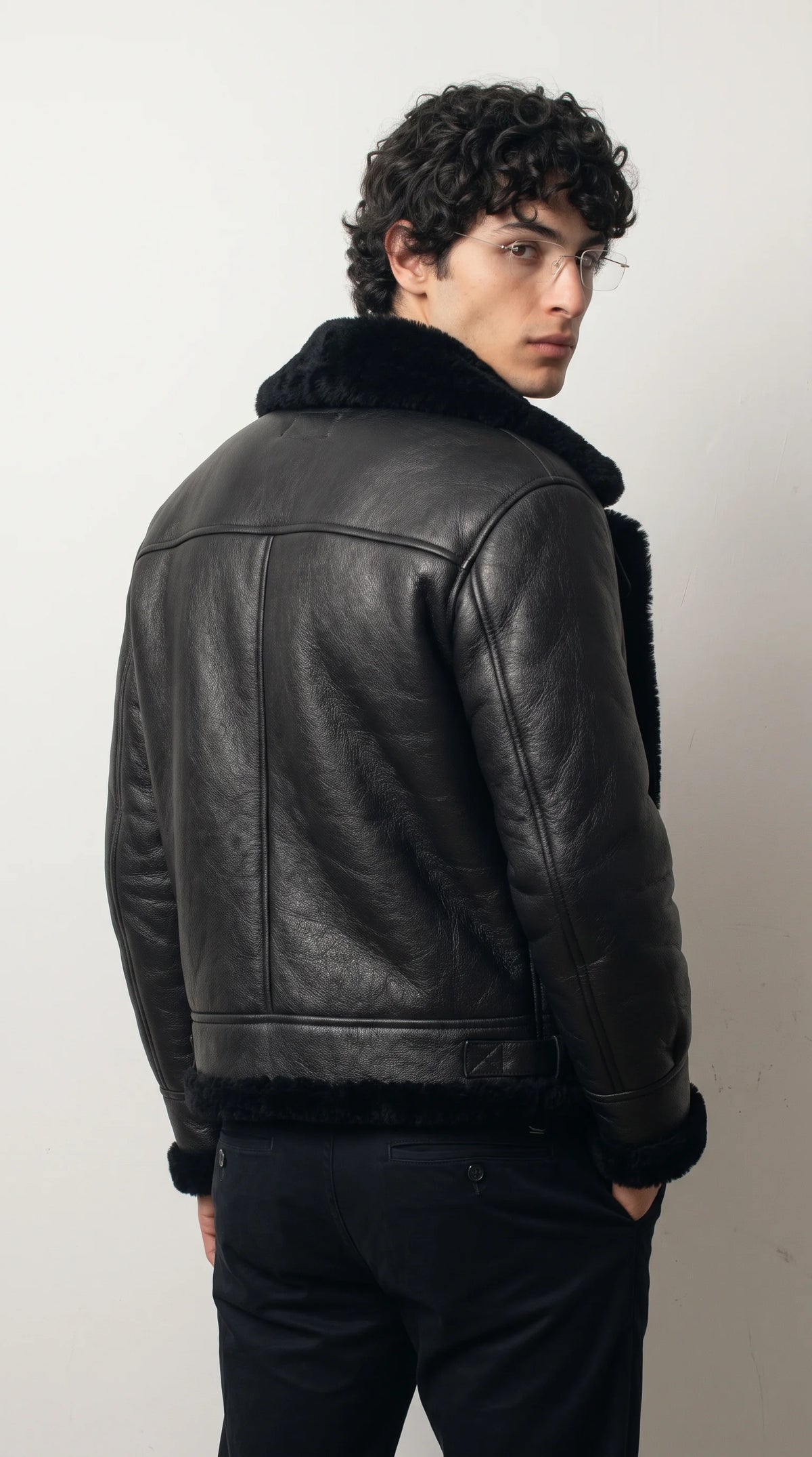 Black genuine leather flight jacket with a structured shoulder yoke, vertical back panel seams and a thick black faux-shearling hem, creating a defined waist-length silhouette with rugged heritage aviator character.