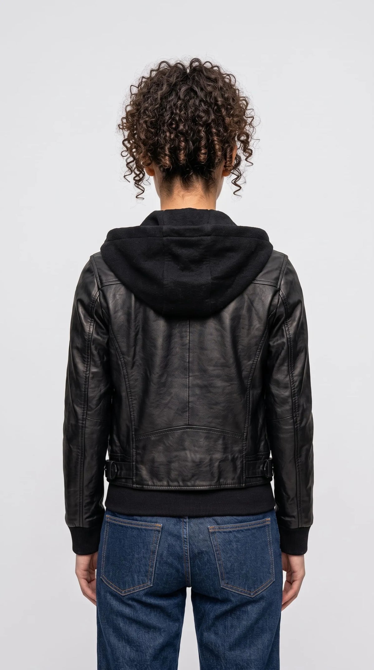 Black genuine leather hooded bomber with a sculpted hood, structured shoulder yoke, vertical back panel seams and a wide ribbed waistband, delivering a clean cropped silhouette for minimalist urban outfits and modern alternative fashion.