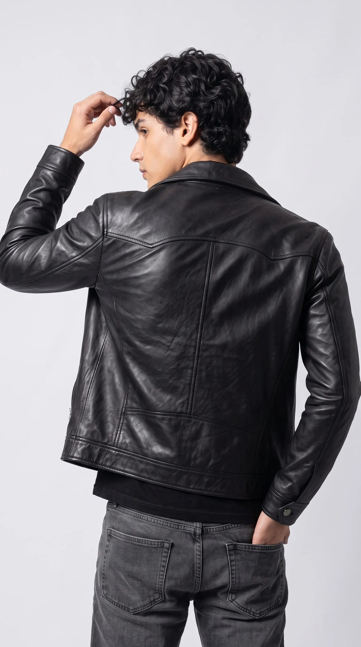 Deep-black genuine leather jacket with a curved upper-back yoke, defined vertical panel seams, dropped shoulders and a relaxed baggy cut, styled with faded charcoal denim. The carefully shaped leather panels add structure without losing the loose silhouette, creating a modern vintage-moto look for relaxed streetwear, layered everyday outfits and understated alternative fashion.