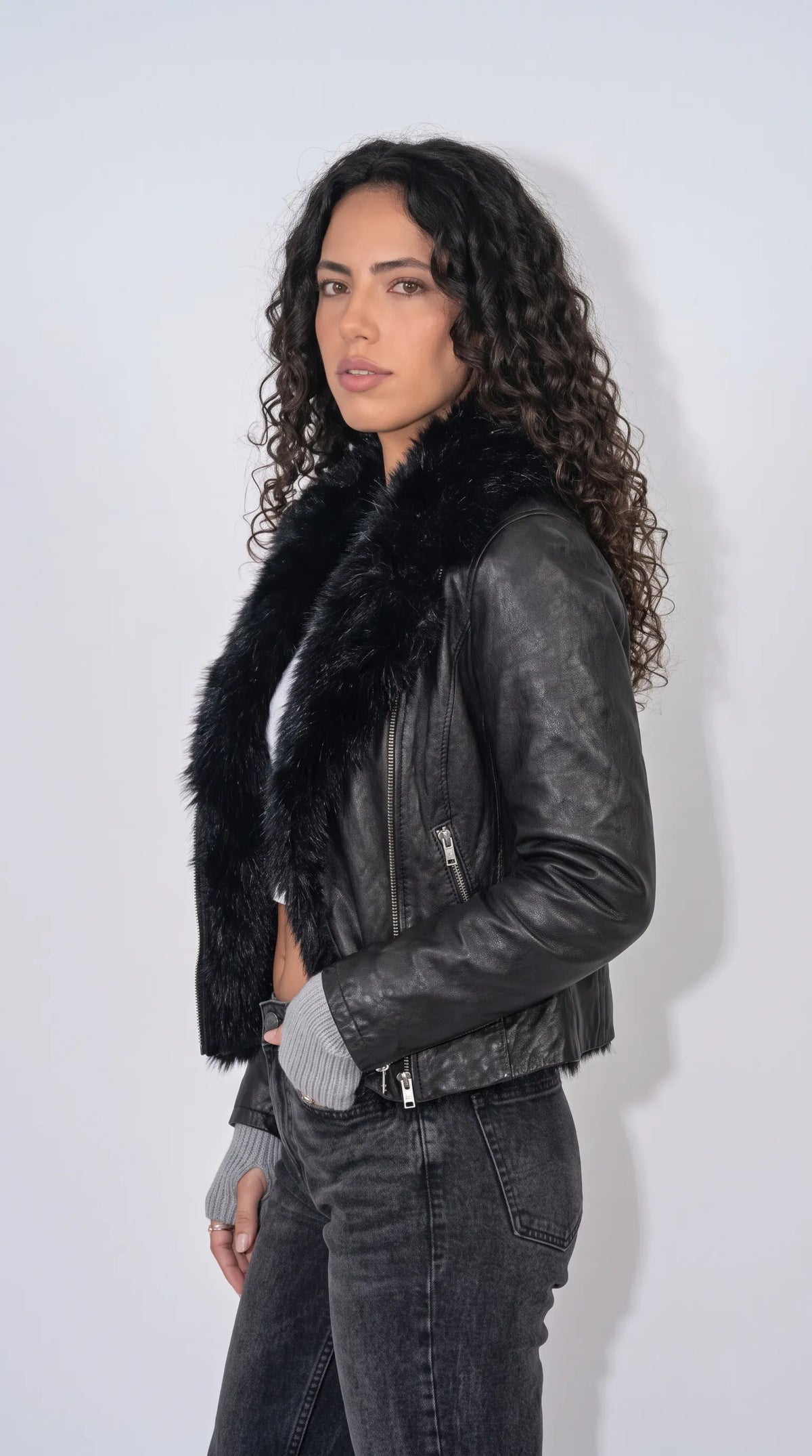 Jet-black leather moto jacket with an oversized faux-fur collar, elongated vertical zip pockets, metal sleeve-cuff zippers and an angular asymmetrical closure, delivering a sharp motorcycle-inspired silhouette for modern alternative fashion.