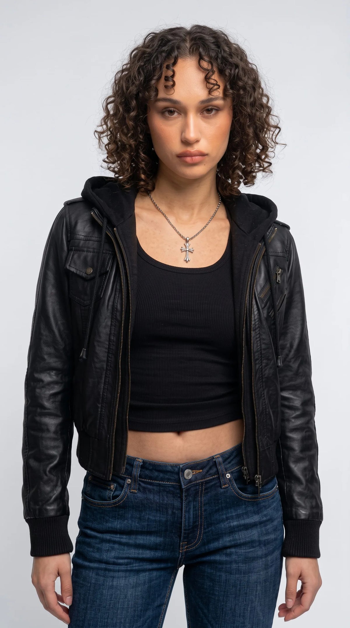 Black genuine leather Y2K bomber jacket with an integrated black fleece-lined hood, adjustable drawstrings, semi-matte leather finish and ribbed cuffs, styled with a black ribbed tank top and dark denim for a bold urban streetwear look.