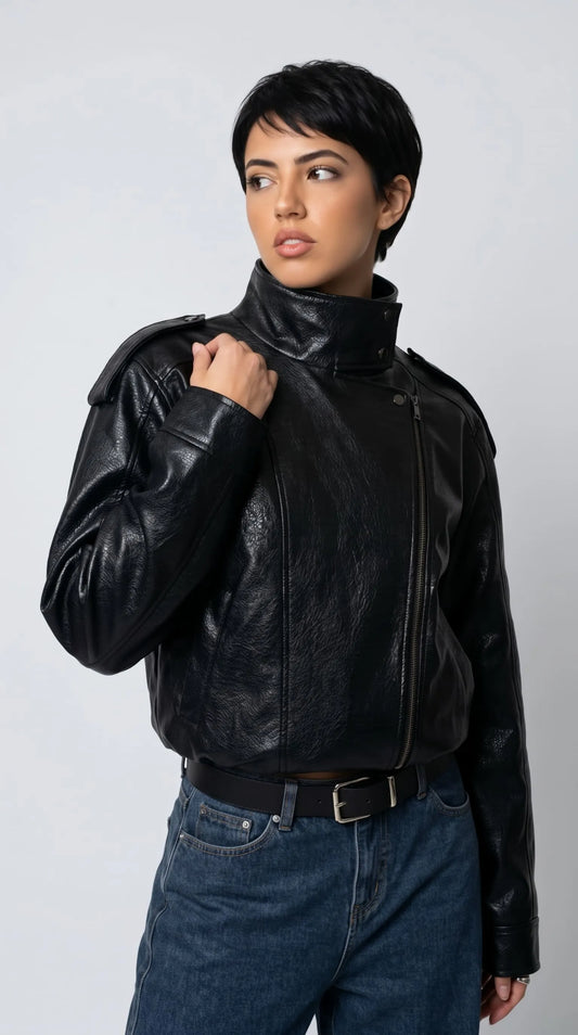 A bold black textured leather oversized jacket styled with blue denim jeans, featuring a dramatic wrap-around high neck, asymmetrical zip closure and relaxed sleeves for a modern alternative streetwear look.