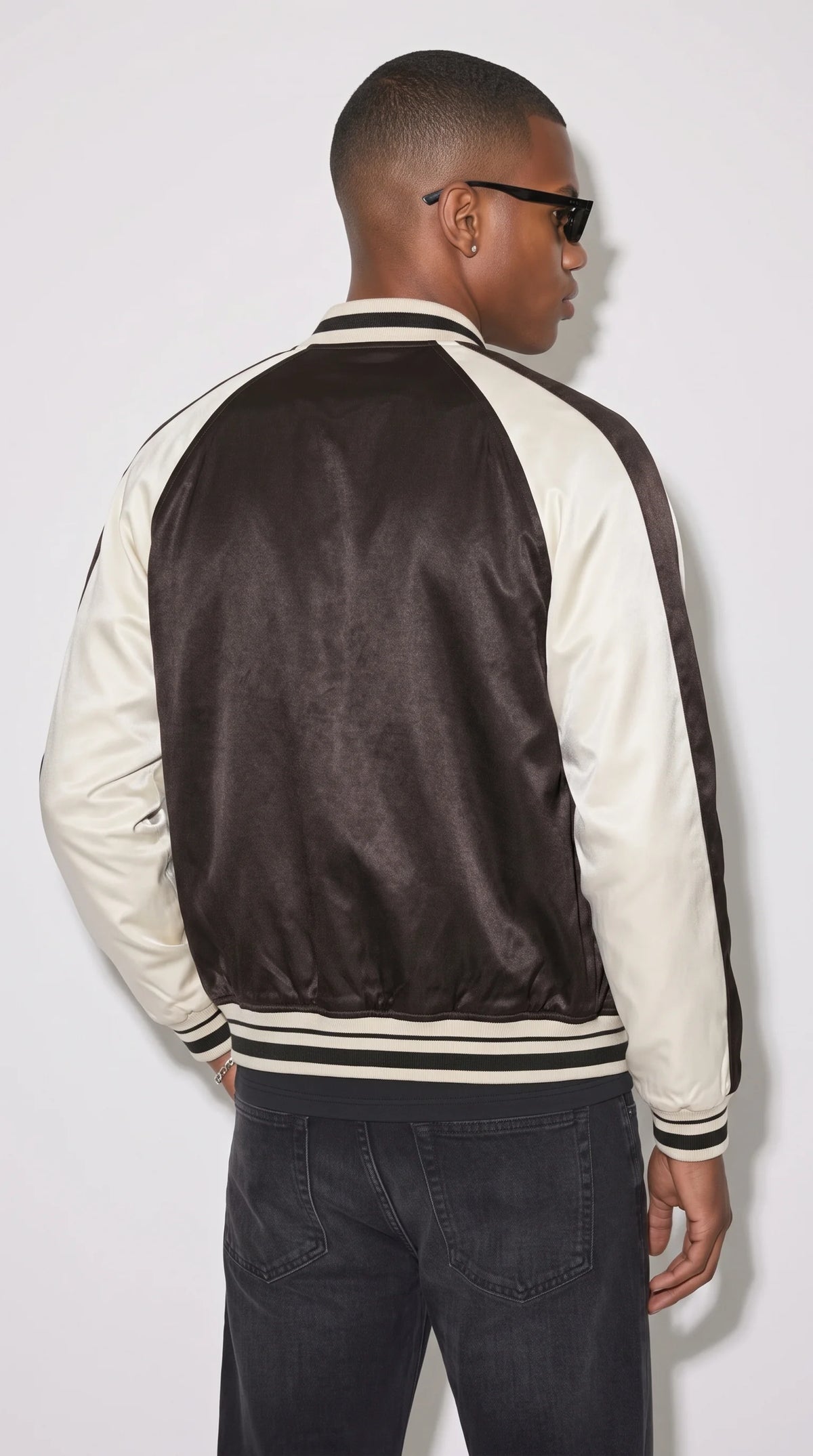 Black varsity jacket with a smooth dark back panel, bright white contrast sleeves and traditional black-and-white striped ribbing around the collar and waistband. Its uncluttered baseball-jacket design keeps the focus on the bold two-tone colour scheme and structured shoulder lines, creating a versatile monochrome outerwear piece for minimal outfits and vintage-inspired sportswear.