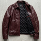 A burgundy leather jacket with a black diamond-quilted lining, laid flat on a textured gray concrete surface.