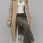 Model wearing an oversized light yellow long cotton overcoat layered over a neutral casual outfit.