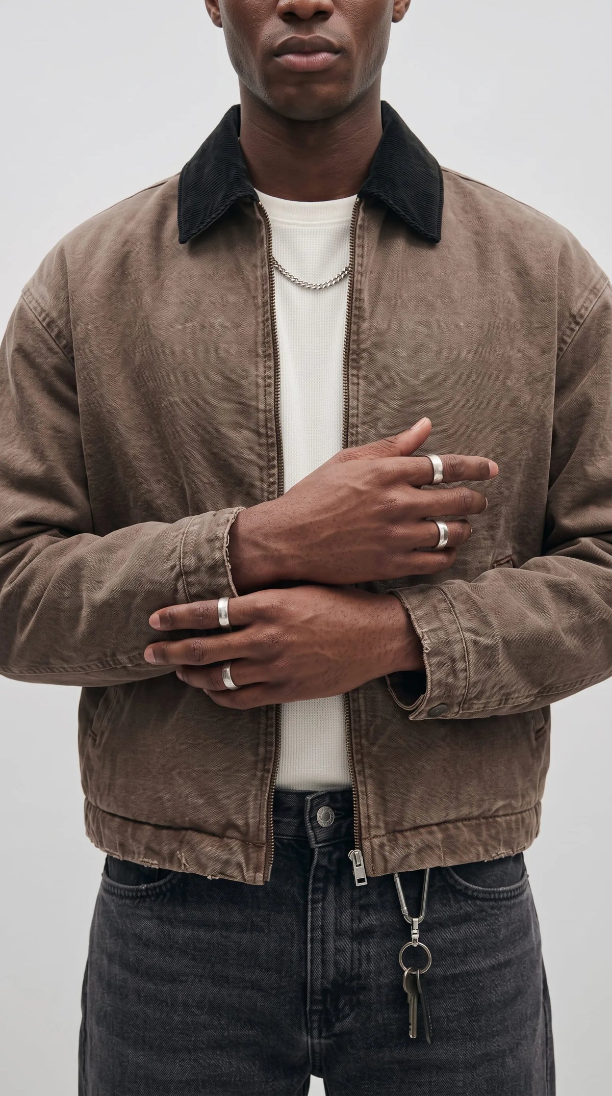 Detail of a washed brown cotton canvas jacket highlighting its charcoal corduroy point collar, sturdy metallic zip fastening, subtle faded fabric character and clean stitched construction for premium casual utility fashion.