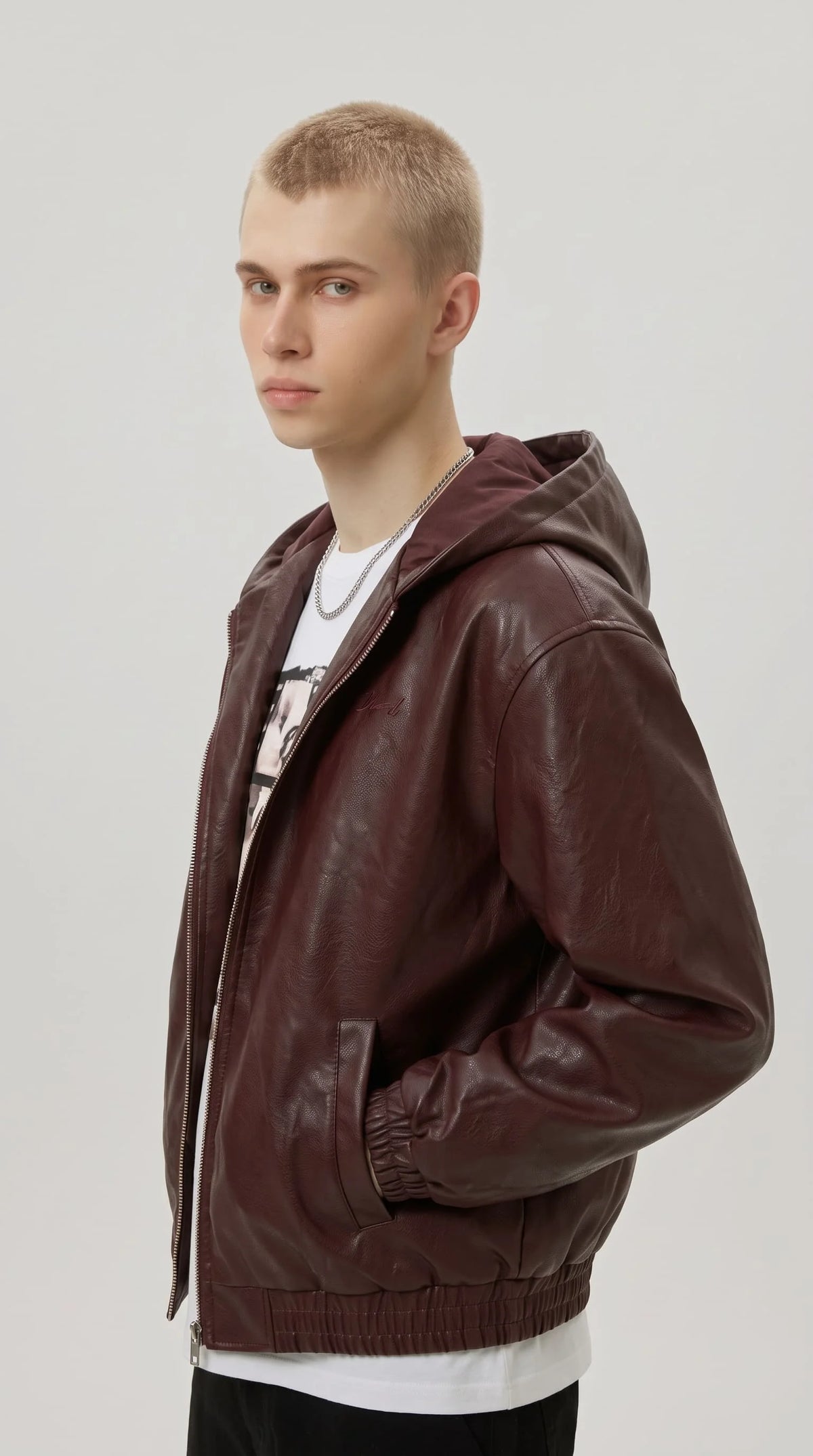 Men's burgundy faux leather hooded bomber jacket with zip front and elastic hem, styled over a white graphic t-shirt