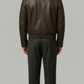 Man wearing a brown leather jacket and dark pants on a gray background