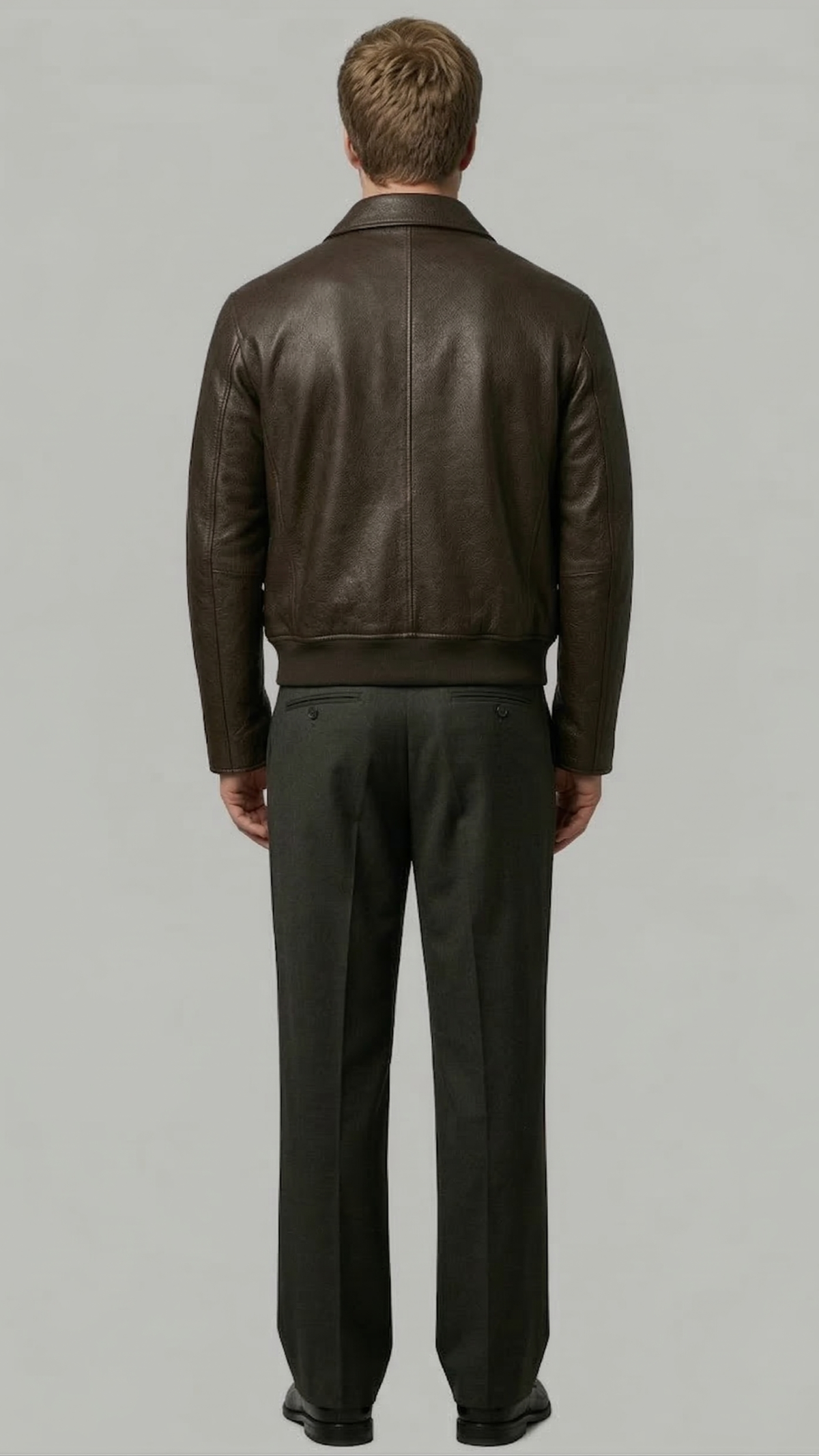 Man wearing a brown leather jacket and dark pants on a gray background