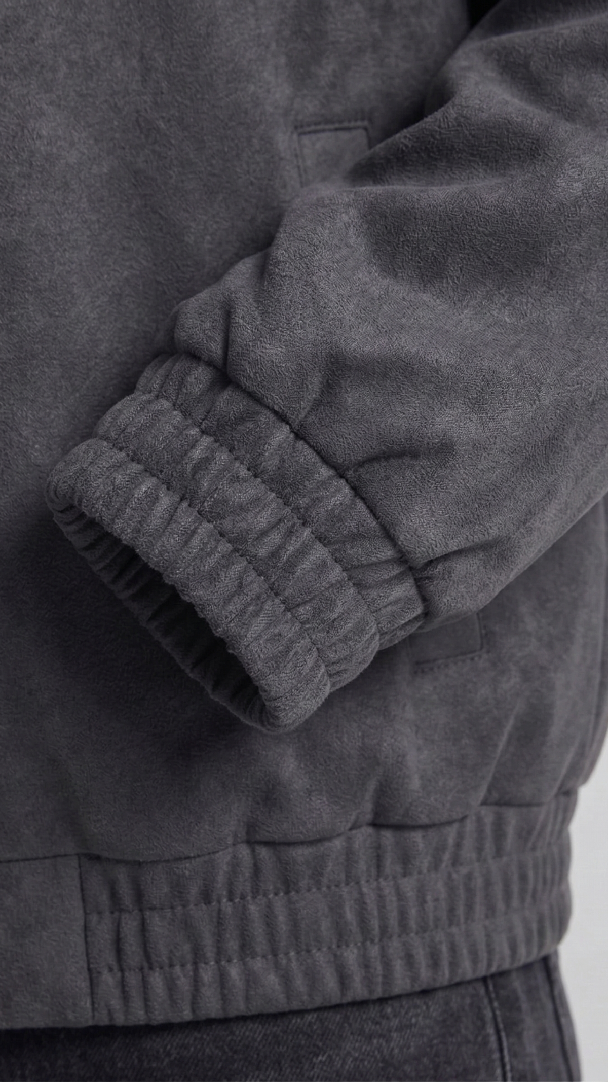 Close-up of a dark gray suede jacket with a focus on the sleeve and waistband.