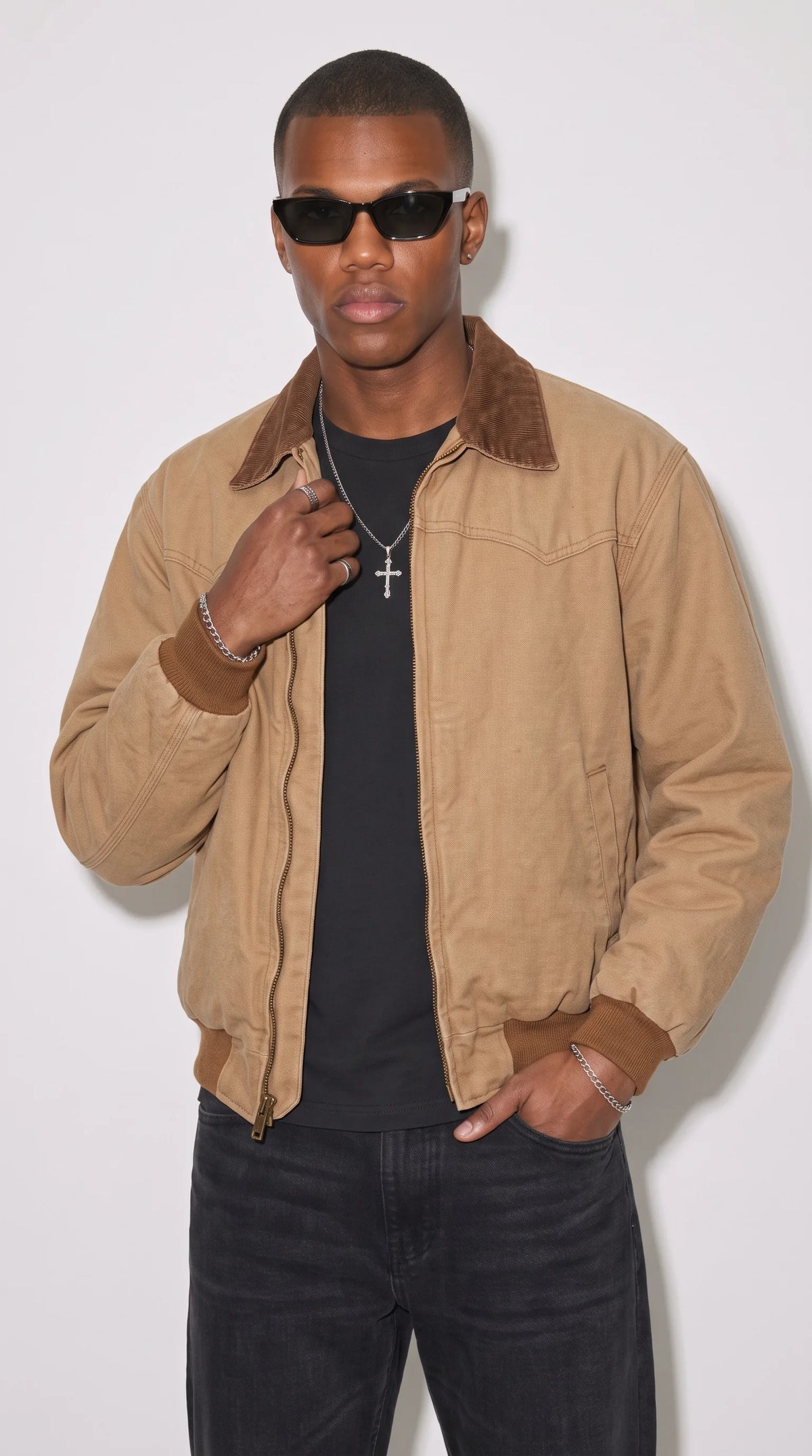 Men’s light camel-brown cotton bomber jacket with a dark-brown corduroy-style pointed collar, matching rib-knit cuffs and waistband, and a full-length metal zipper, styled with a black T-shirt and dark jeans for a clean casual streetwear outfit.