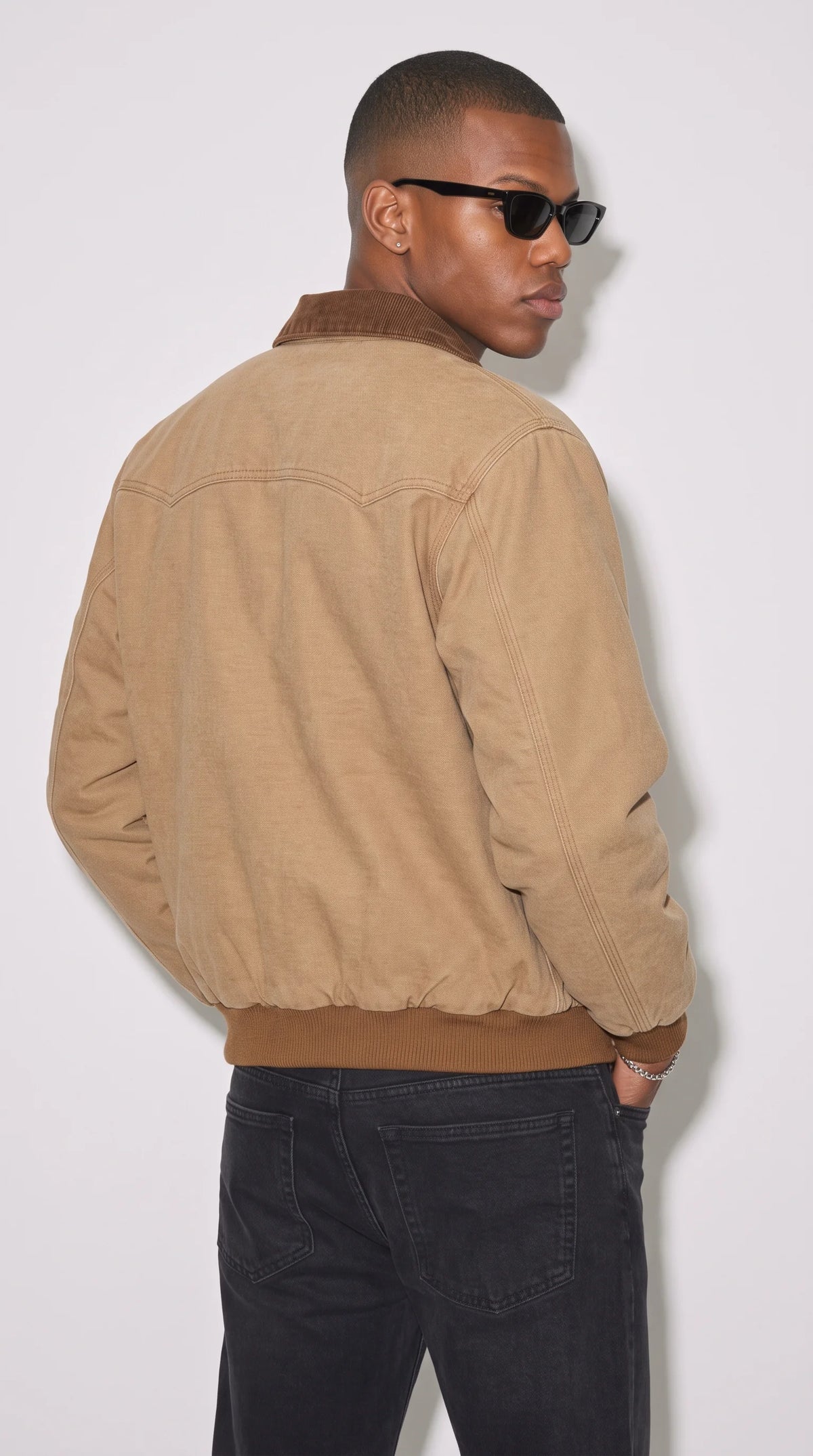 Camel-brown cotton jacket with defined shoulder-yoke seams, reinforced stitching, a traditional dark-brown pointed collar and a matching ribbed waistband, highlighting its structured construction and relaxed bomber silhouette for modern workwear-inspired outfits.